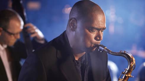 A close up of a man with his eyes closed, playing a saxaphone at a Jazz club in Ten Trinity