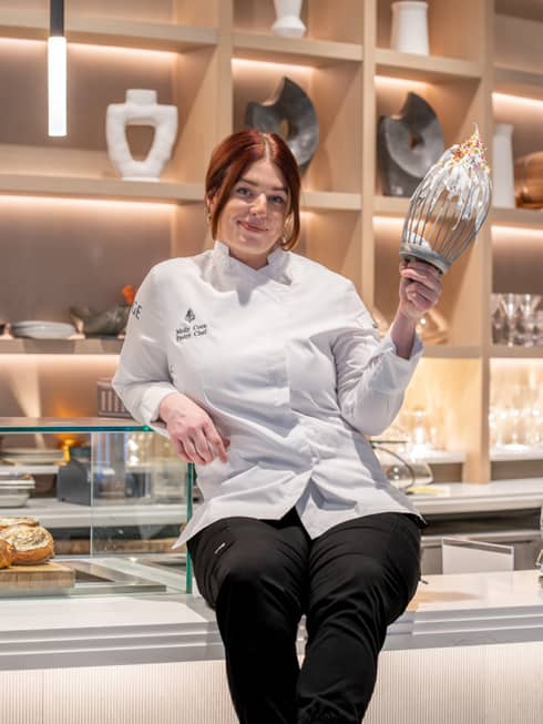 Chef Molly Coen in a kitchen holding a whisk.