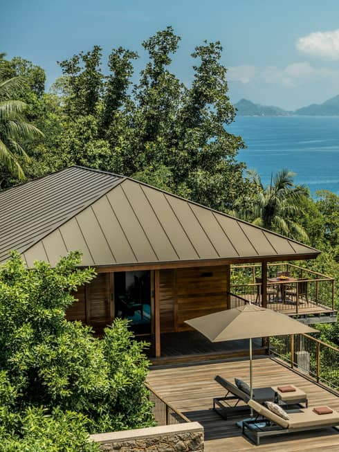 View over wood patio, villa roof on green mountain slope, blue ocean in background
