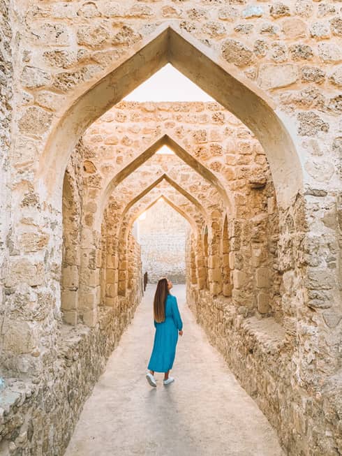 A woman stands underneath a stone pathway.