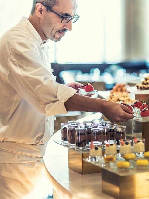 A chef prepares several chocolate pastries inside a patisserie.