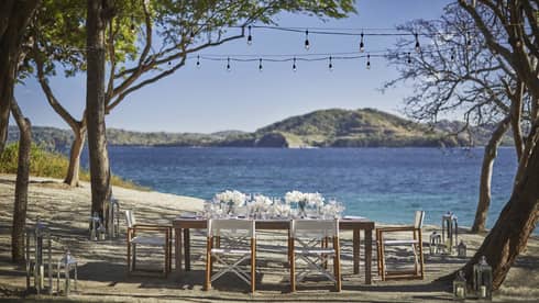 Outdoor dining table with white flowers on sunny beach by ocean