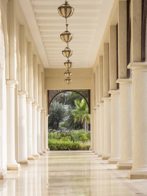 Outdoor beige marble walkway lined with tall columns and garden view at far end