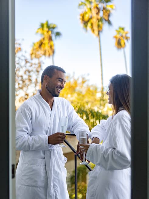Man and woman both wearing bath robes and holding wine glasses, standing on the terrace.