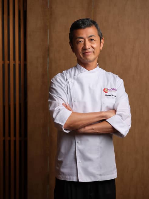Person in white chef's coat stands with arms crossed