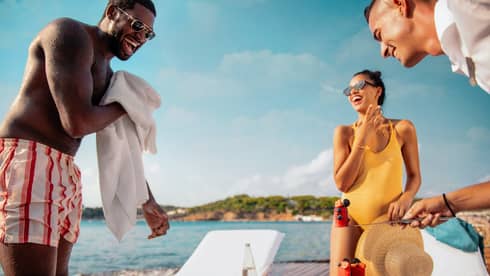 Three friends enjoying a sunny day on waterfront sundeck with white lounge chairs