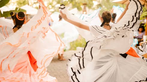 Two women dressed in multi-layered dresses with ruffls along the hem dance on a patio