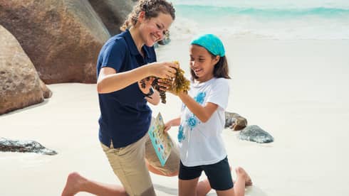 A WiseOceans female employee teaches a young girl about ecology on a beach
