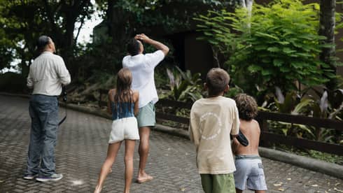 Two adults and three children look up into the trees