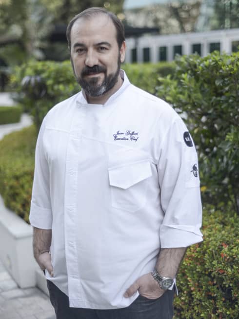 Chef Juan Gaffuri stands in front of some foliage.