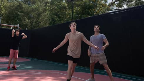 Three teenage boys play basketball on an outdoor court