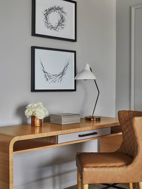 Retro-style leather chair, wood desk with white roses, lamp under framed prints