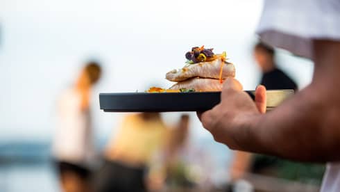 Close-up of server carrying tray with two thick, grilled fish fillets with edible flower garnish