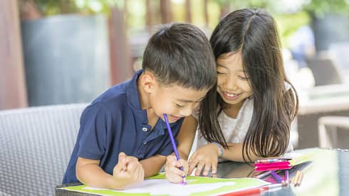 Smiling young boy and girl colouring in book with crayon