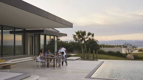 Family dining outdoors on a modern patio by the pool, with a scenic view of mountains and desert plants at sunset, creating a serene and intimate setting.
