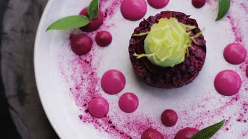 Beetroot Tartare on white plate surrounded by beetroot powder and beetroot spheres