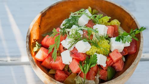Diced watermelon and feta salad garnished with parsley and dill in wooden bowl