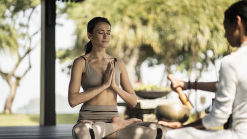 A woman sitting outside doing a yoga breathing pose.