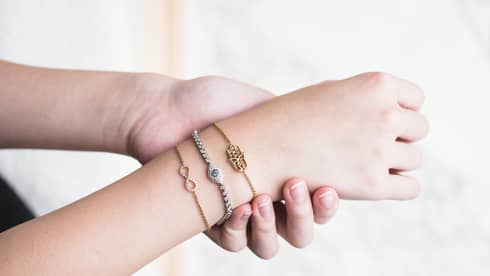 Three delicate bracelets adorn a person's wrist that is being held by another hand