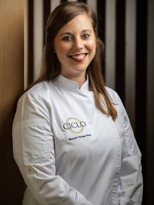 A female chef with long brown hair in white chef clothes that say "Ciclo".