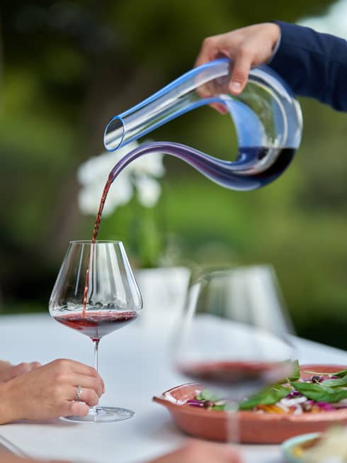Hand pouring red wine in decanter into a wine glass