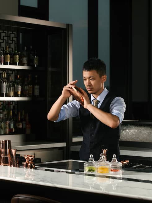 William Zhang, bartender, behind the counter shaking a cocktail