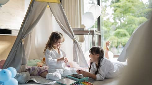 Two girls play in an in-room kids tent with white balloons
