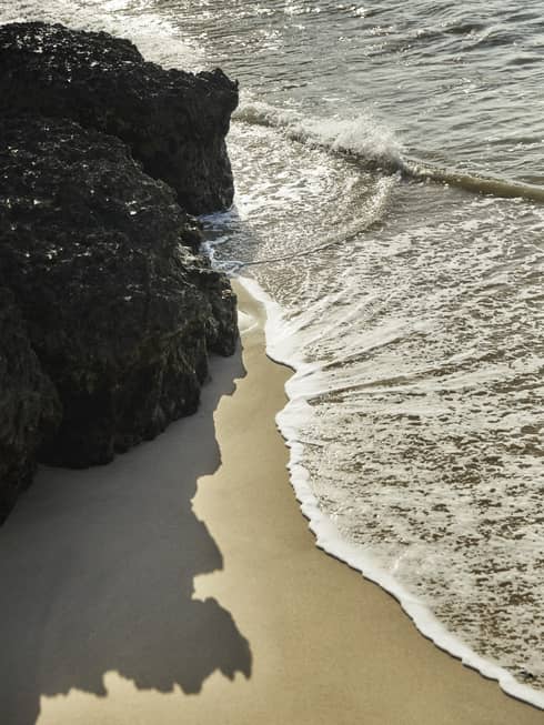Calm waves brush up against a smooth beach and nearby rock