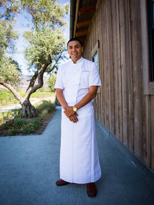 A chef in a long chefs coat standing outside.