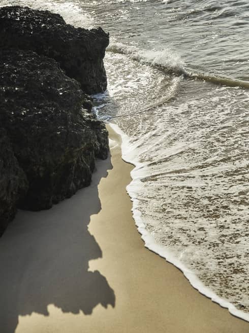 Calm waves brush up against a smooth beach and nearby rock