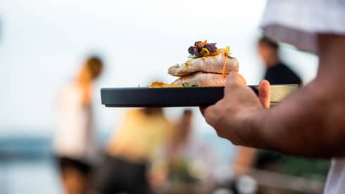 Close-up of server carrying tray with two thick, grilled fish fillets with edible flower garnish