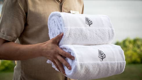 Close-up of hotel service staff carrying two rolled white towels with Four Seasons logo