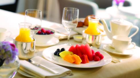 Close-up of in-room dining table service with plate of fresh melon and berries, tea and orange juice