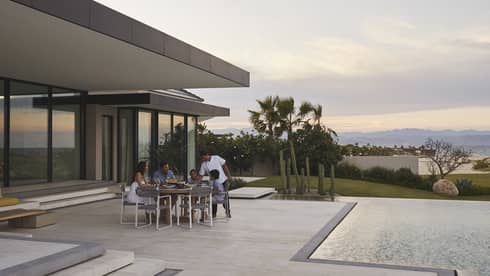 Family dining outdoors on a modern patio by the pool, with a scenic view of mountains and desert plants at sunset, creating a serene and intimate setting.