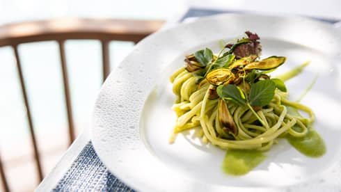 Pasta with green sauce, garnished with salad greens served on white plate