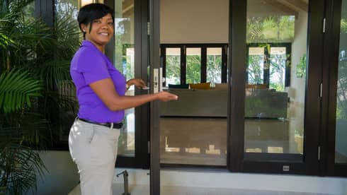 Smiling villa ambassador holds open glass door to estate