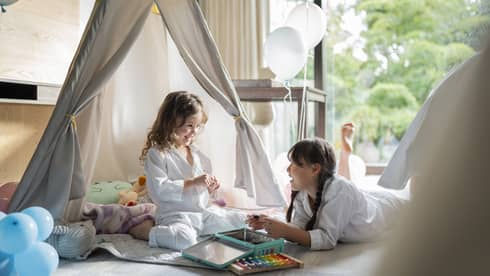 Two girls play in an in-room kids tent with white balloons