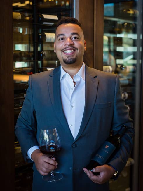 A man holding a glass of wine in a dark grey suit.