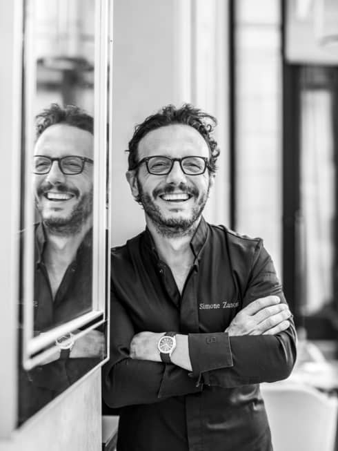 Shot of Chef Simone Zanoni, smiling next to a wall with mirror