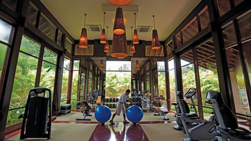 Man rolls blue pilate balls in sunny Fitness Centre with cardio machines