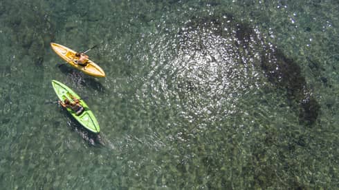 Aerial view of man and woman in green and orange kayaks on reef