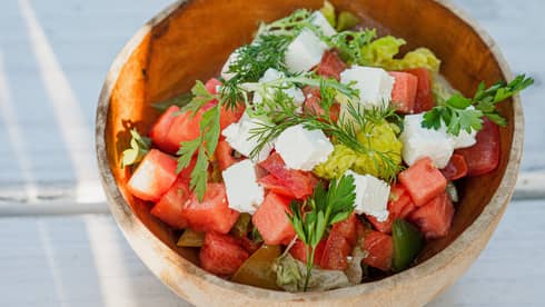 Diced watermelon and feta salad garnished with parsley and dill in wooden bowl