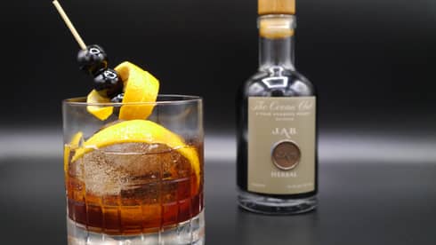 National Rum Day Cocktail with orange peel garnish in rock glass, small bottle on bar