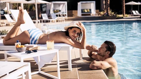 Guest laying in a lounge chair by the pool while the other guest stands in the pool.