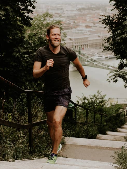 Front view of a runner on a hilltop staircase in morning light, a backdrop of old-world architecture along the harbour below.