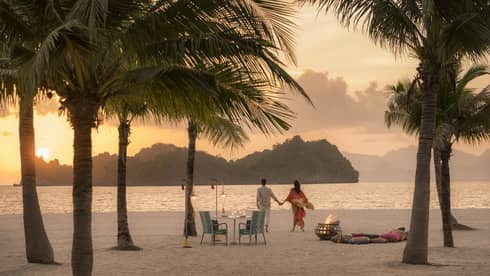 A man and woman on a beach having a Punta chintai private dinner at Four Seasons Langkawi