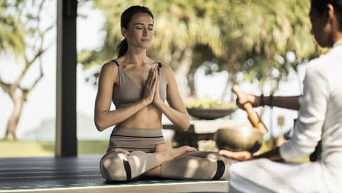 A woman sitting outside doing a yoga breathing pose.
