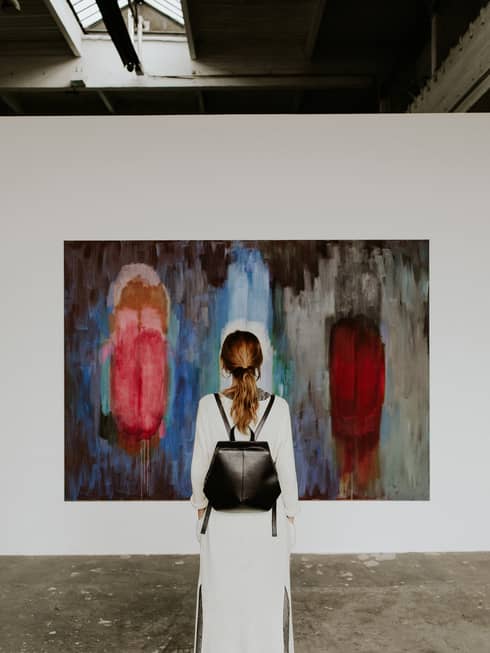 A person with a backpack standing in front of an abstract painting in an art gallery.