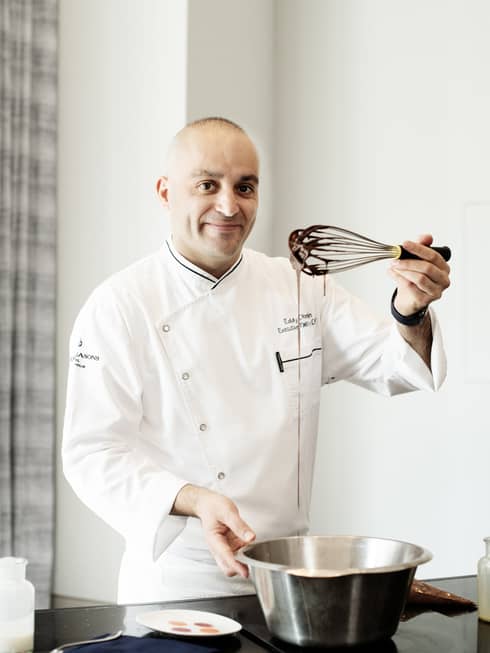Chef Eddy Dhenin holding a bowl and a whisk in a kitchen