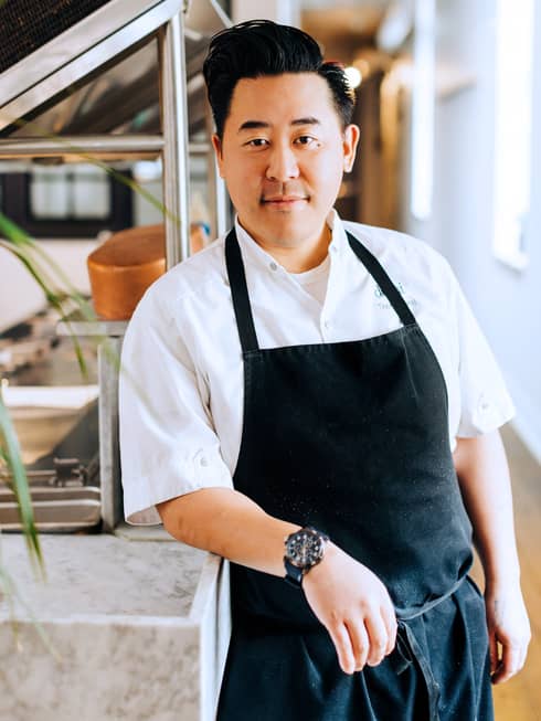 Chef Thony Yang wearing an apron and leaning on a table in a kitchen